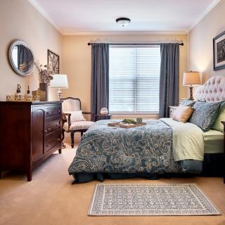 A cozy bedroom with elegant decor, featuring a bed, dresser, mirror, and lamps.