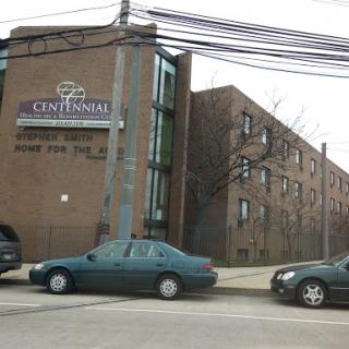 An urban scene featuring a building with a sign for 'Centennial' and parked cars along the street.