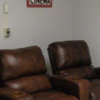 A cozy home theater setup with leather recliner chairs and a cinema sign on the wall.