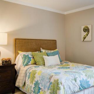 A cozy bedroom with a neatly made bed, featuring colorful bedding and pillows, a bedside lamp, and a decorative painting on the wall.