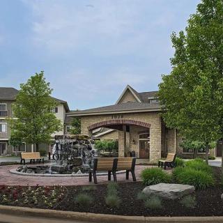 A landscaped outdoor area featuring a fountain, seating, and nearby buildings.