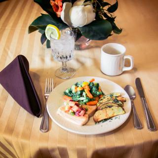 An elegantly set table with a plate of salmon and vegetables, accompanied by a glass of water and coffee.