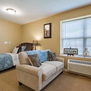 A cozy bedroom with a sofa, bed, and window providing natural light.