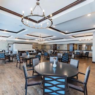 A spacious and elegantly designed dining area with multiple tables and chairs, featuring chandeliers and a wooden floor.