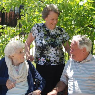 Three elderly people enjoying a conversation outdoors on a sunny day.