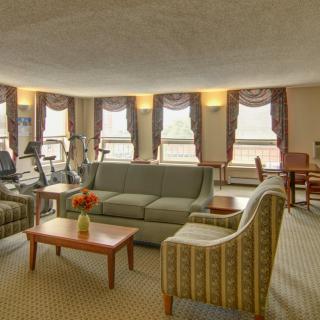 A spacious living room with exercise equipment, featuring comfortable sofas and large windows adorned with curtains.