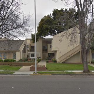 A suburban residential apartment building with trees and a sidewalk in front.