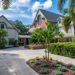 A beautiful suburban home surrounded by lush tropical landscaping and a clear blue sky.