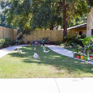 A well-maintained garden with grass, plants, and decorative sculptures bordered by a wooden fence.