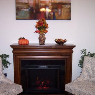 A cozy indoor setting featuring a decorative fireplace adorned with autumn-themed decorations, including a vase of flowers and a small pumpkin.