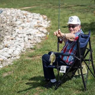 An elderly man sitting on a chair by the water, enjoying a day of fishing.