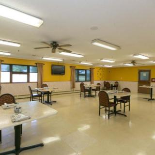 A spacious indoor dining area with tables and chairs, illuminated by bright ceiling lights.