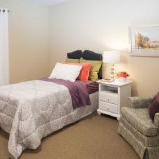 A cozy bedroom with a neatly made bed, nightstand, and comfortable chair.