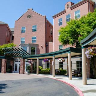 A multi-story brick building with a covered entrance surrounded by greenery.