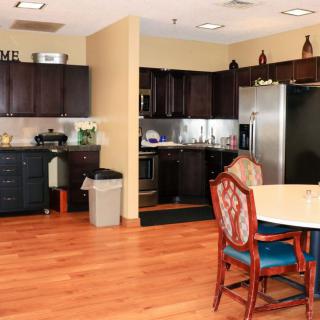 A modern kitchen with dark cabinets, stainless steel appliances, and a small dining area featuring hardwood flooring and upholstered chairs.