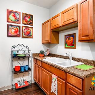 A cozy kitchen with wooden cabinets, colorful artwork, and neatly arranged shelves.