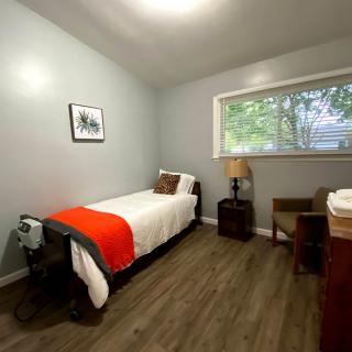 A minimalist bedroom with a single bed, wooden floors, and a desk by the window.
