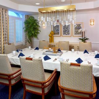 A formal dining room setup with a large table, upholstered chairs, and an elegant chandelier.