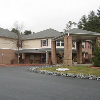 A two-story brick building with a covered entrance and surrounding greenery.