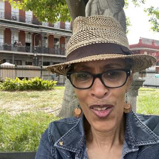 A cheerful woman enjoying a sunny day in the park, wearing a stylish hat and glasses.