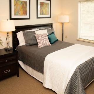 A cozy bedroom with a neatly made bed, accented by artwork and soft lighting.