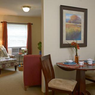 A cozy apartment interior featuring a small dining area with a table and chairs, and a comfortable living room.