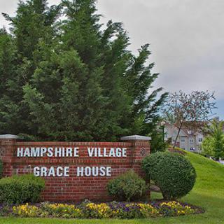 Entrance sign for Hampshire Village and Grace House surrounded by trees and greenery.