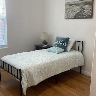 A cozy and minimalist bedroom featuring a single bed with light bedding and a bedside lamp.