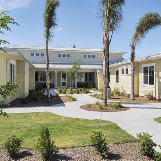 A modern residential building with a landscaped garden and palm trees on a sunny day.