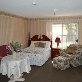 A cozy bedroom with a bed, floral-patterned furniture, and a small table in a well-lit room.