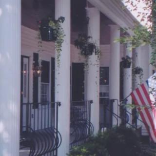 A traditional porch with white columns, hanging plants, and an American flag.