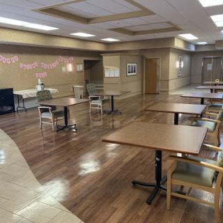 A spacious and empty dining hall featuring wooden floors, tables, and chairs, ready for an event or gathering.