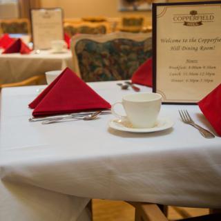 A neatly arranged dining table in a restaurant with a menu, cup, saucer, and red folded napkins.