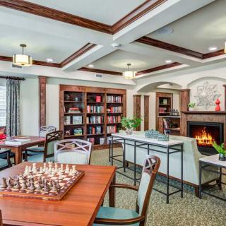 A cozy library room with bookshelves, a fireplace, and tables set up for chess.