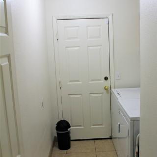 A compact laundry room with a washer, dryer, and a small trash can next to a white door.