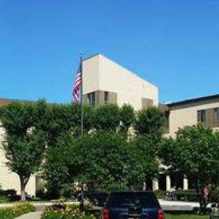 A building with an American flag, surrounded by trees and a parked car under a clear blue sky.