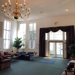 A spacious lobby with a grand chandelier, ample seating, and natural light streaming through large windows.
