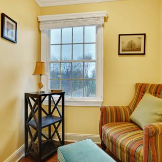 A cozy corner in a living room with an armchair next to a window, featuring a side table with a lamp.