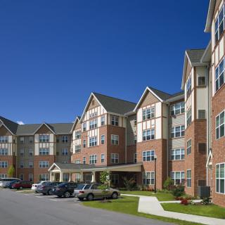 A multi-story residential apartment building with a parking area in front under a clear blue sky.