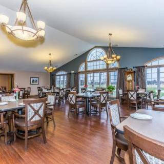 A spacious and elegantly decorated dining area with wooden floors, featuring multiple tables and chairs, large windows, and chandeliers.