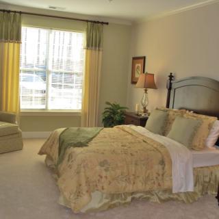 A cozy and elegantly decorated bedroom featuring a large bed with floral bedding, a window with curtains, and a comfortable armchair.