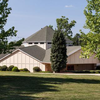 A suburban house surrounded by trees and a well-kept lawn on a sunny day.