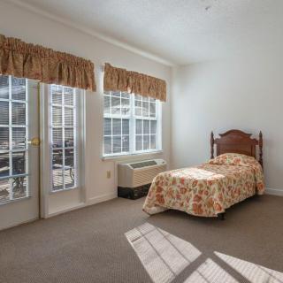 A cozy bedroom with a single bed and large windows letting in sunlight.
