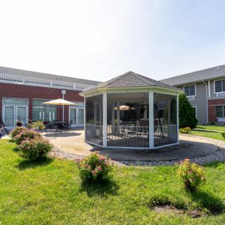 A charming gazebo situated in a landscaped garden area with a surrounding lawn and adjacent building.