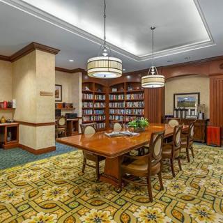 A cozy library reading room with a large wooden table and chairs surrounded by bookshelves.