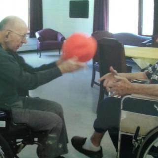 Elderly individuals playing with a ball while seated in wheelchairs indoors.