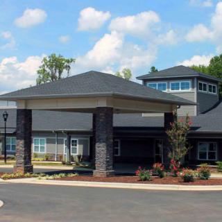 A modern building with a covered entrance and landscaped surroundings under a partly cloudy sky.