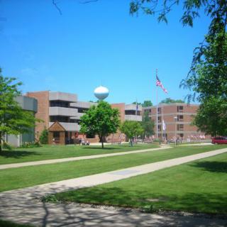 A sunny day at a campus with buildings, trees, and an American flag.