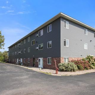 A modern three-story apartment building with a gray exterior and brick accents under a clear blue sky.