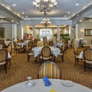An elegant dining room with neatly arranged tables and chairs, featuring a prominent chandelier.